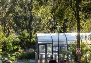 Familie går på sti ved glampingstedet Huttopia Lac de la Siauve omgivet af træer og et drivhus.