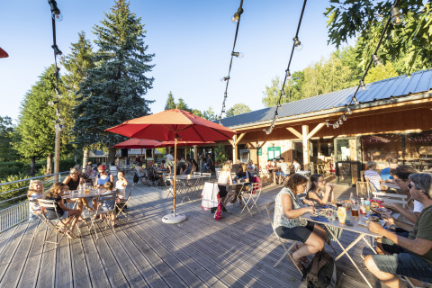 Gäste genießen Mahlzeiten auf der Terrasse bei Huttopia Lac de la Siauve Glamping, umgeben von Bäumen.
