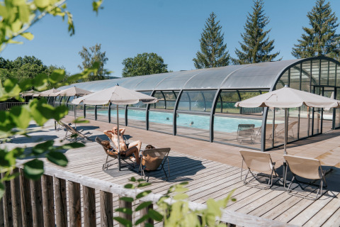 Area piscina all'aperto con lettini e ombrelloni a Huttopia Lac de la Siauve - Glamping Auvergne in estate.