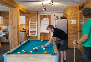 Two people play pool in a cozy, wood-paneled room at Stadslandgoed De Heicohoeve - Glamping Lodges Gelderland.