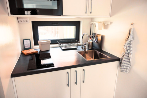 Cocina compacta y moderna en alojamiento glamping Tiny lodge - Ellertshäuser See con fregadero y vitrocerámica.