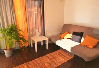 Alojamiento glamping Tiny Lodge - Ellertshäuser See con sofá, cojines, planta y luz solar en el interior.