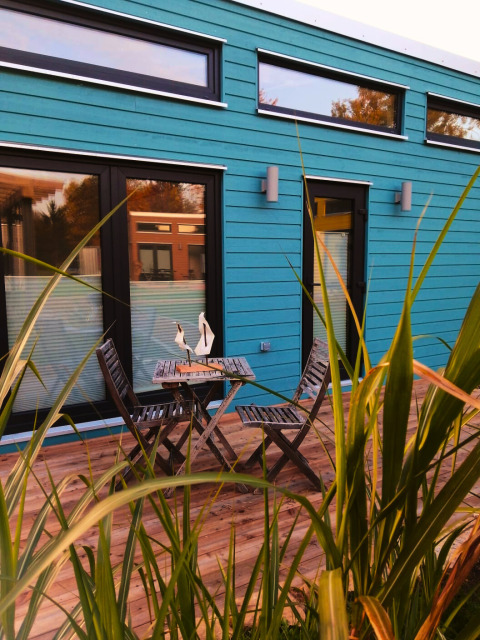 Terrazza all'aperto con tavolo e sedie di legno davanti a un tiny lodge turchese per glamping a Ellertshäuser See.