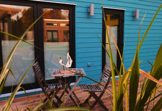 Terrasse extérieure en bois avec table et chaises devant un tiny lodge turquoise au glamping Ellertshäuser See.
