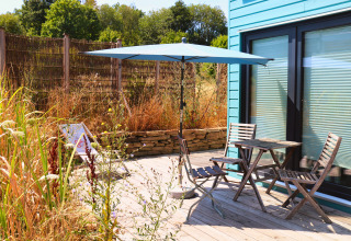 Udendørs terrasse ved Tiny lodge - Ellertshäuser See med blå parasol, træmøbler og vild beplantning.