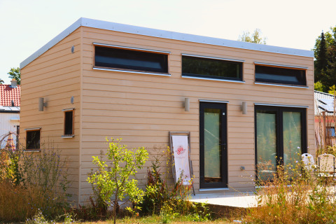 Tiny lodge moderne à Ellertshäuser See, hébergement glamping avec grandes fenêtres et façade en bois beige en été.