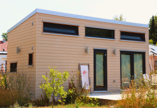 Moderne Tiny Lodge am Ellertshäuser See, Glamping-Unterkunft mit großen Fenstern und hellem Holzdesign im Sommer.