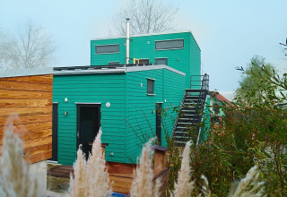 Grøn glampingbolig kaldet Tiny lodge - Ellertshäuser See med træfacade og udendørs trappe i naturen.