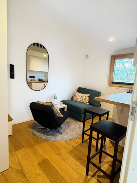 Moderne tiny lodge aan Ellertshäuser See met zithoek, kitchenette, barkrukken en groot raam.