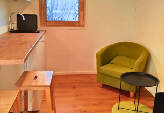 Alojamiento glamping en Tiny lodge - Ellertshäuser See con cocina moderna, sillón verde y ventana.