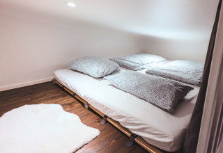 Moderne glamping, Tiny lodge - Ellertshäuser See med lavt loft, dobbeltseng og hyggeligt tæppe på trægulv.