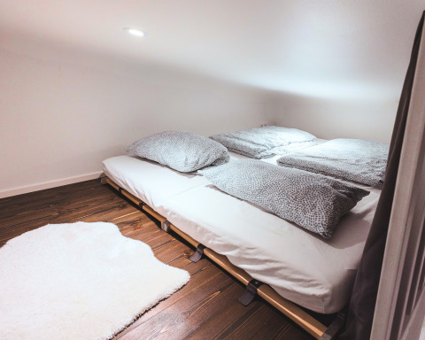 Knusse glamping Tiny lodge - Ellertshäuser See met laag plafond, tweepersoonsbed en wit kleed op houten vloer.