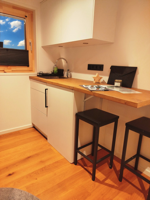 Cucina moderna in una tiny lodge con piano in legno, sgabelli neri e finestra che guarda il cielo.