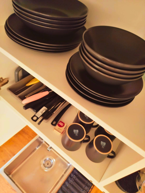 Black tableware and cutlery neatly arranged in a kitchen cabinet at Tiny lodge - Ellertshäuser See glamping site.