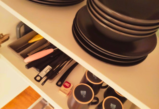 Vajilla y cubiertos negros ordenados en un armario de cocina del glamping Tiny lodge - Ellertshäuser See.