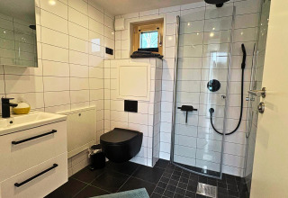Moderne badkamer met zwart toilet, douche en witte tegels in Tiny Lodge bij Ellertshäuser See voor glamping.