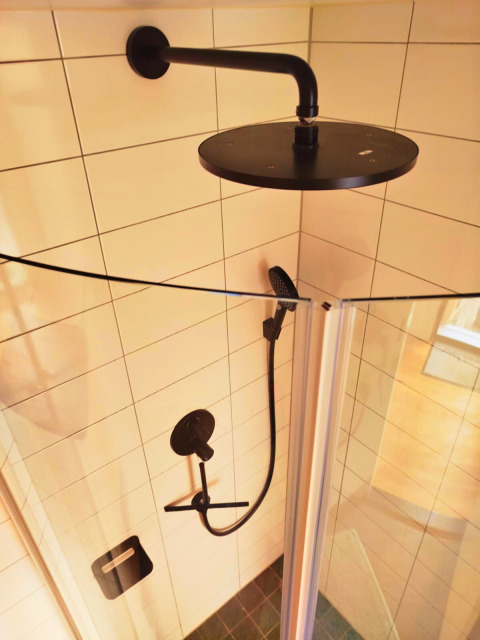 Moderne douche met zwarte kranen in Tiny lodge Ellertshäuser See glamping, lichte betegelde badkamer.