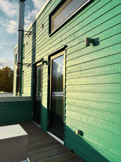 Vista exterior de Tiny Lodge en Ellertshäuser See con paredes verdes de madera y terraza moderna para glamping.