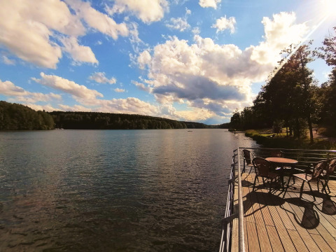 Belle vue sur le lac depuis une terrasse en bois au Tiny lodge - Ellertshäuser See avec tables et chaises au soleil.