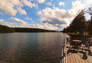 Belle vue sur le lac depuis une terrasse en bois au Tiny lodge - Ellertshäuser See avec tables et chaises au soleil.