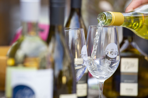 White wine being poured into glasses at Tiny Lodge - Ellertshäuser See, surrounded by bottles, outdoor setting.