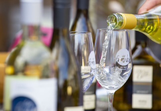 Du vin blanc versé dans des verres au Tiny lodge - Ellertshäuser See, entouré de bouteilles, ambiance conviviale.