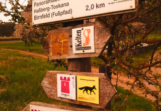 Trail signs for hiking routes at Haßberg-Toskana, Birnfeld, surrounded by blooming trees in spring scenery.
