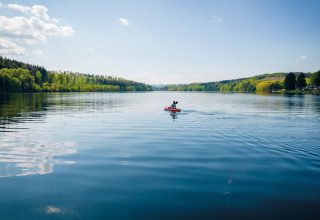 Persona en kayak en el lago tranquilo de Vakantiepark Sorpesee - Boomhutten Noordrijn-Westfalen, rodeado de bosque.