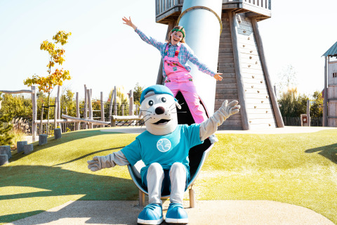 Divertimento al parco giochi di Strandpark De Zeeuwse Kust, mascotte e bimbo che giocano sullo scivolo.