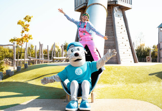 Speelplezier bij Strandpark De Zeeuwse Kust, mascotte en kind samen glijdend van de glijbaan in de buitenlucht.