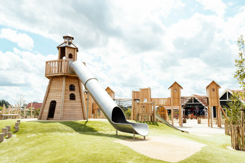 Parque infantil con tobogán y torres de madera en Strandpark De Zeeuwse Kust - Safaritenten Zeeland bajo cielo nublado.