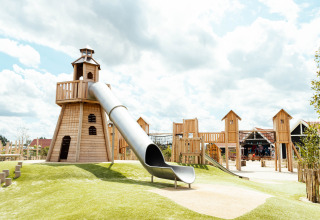 Parque infantil con tobogán y torres de madera en Strandpark De Zeeuwse Kust - Safaritenten Zeeland bajo cielo nublado.