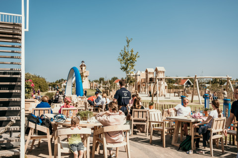 Buitenzitgedeelte bij Strandpark De Zeeuwse Kust met speeltuin op de achtergrond tijdens een zonnige dag.