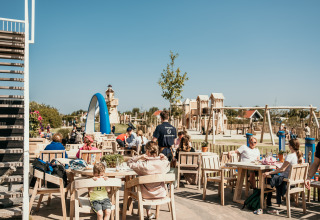 Udendørs siddeområde på Strandpark De Zeeuwse Kust med legeplads i baggrunden på en solrig dag.
