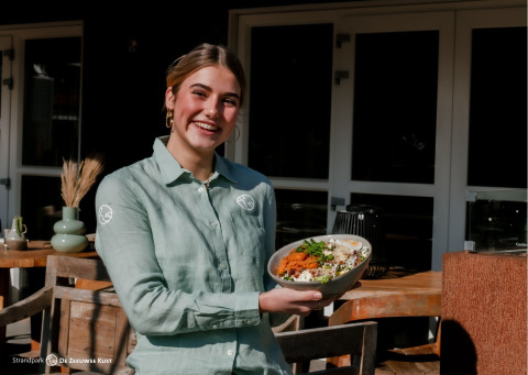 Lächelnde Frau im Restaurant serviert ein Gericht bei Strandpark De Zeeuwse Kust - Safaritenten Zeeland.