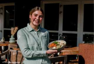 Lächelnde Frau im Restaurant serviert ein Gericht bei Strandpark De Zeeuwse Kust - Safaritenten Zeeland.