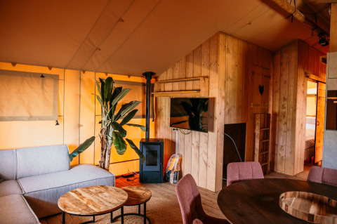 Innenansicht eines luxuriösen Glamping-Safaritents bei Strandpark De Zeeuwse Kust mit Sofa, TV und Holzwänden.