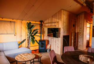 Innenansicht eines luxuriösen Glamping-Safaritents bei Strandpark De Zeeuwse Kust mit Sofa, TV und Holzwänden.