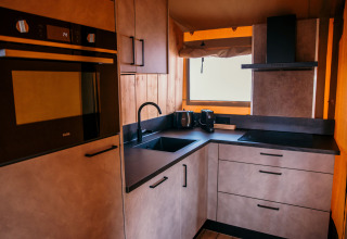 Moderne kitchenette in een glamping safaritent bij Strandpark De Zeeuwse Kust met oven, spoelbak en raam.