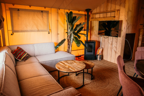 Intérieur d'une tente glamping de luxe au Strandpark De Zeeuwse Kust avec canapé, TV et meubles en bois.
