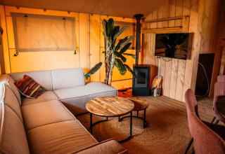 Intérieur d'une tente glamping de luxe au Strandpark De Zeeuwse Kust avec canapé, TV et meubles en bois.