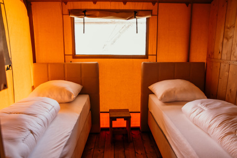 Dos camas individuales con sábanas blancas en una tienda glamping en Strandpark De Zeeuwse Kust - Safaritenten Zeeland.