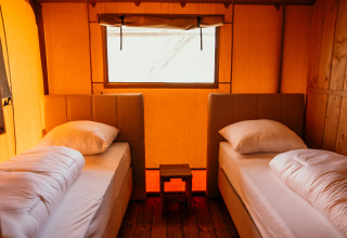 Due letti singoli con biancheria bianca in una tenda glamping al Strandpark De Zeeuwse Kust - Safaritenten Zeeland.