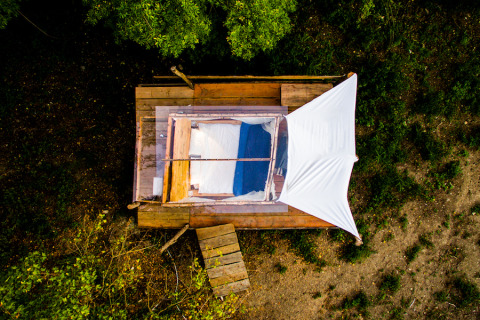Luftfoto af Novanta Skylodge i Italien, glamping på en træplatform med seng og hvidt solsejl i skoven.