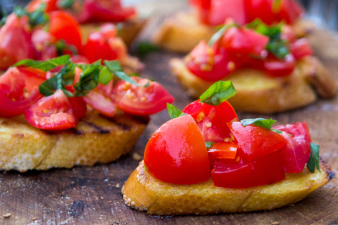 Bruschetta mit frischen Tomaten und Basilikum auf geröstetem Brot, serviert auf einem rustikalen Holztisch.