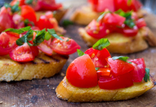 Bruschetta con pomodori freschi e basilico su pane tostato, servita come antipasto su tagliere rustico di legno.