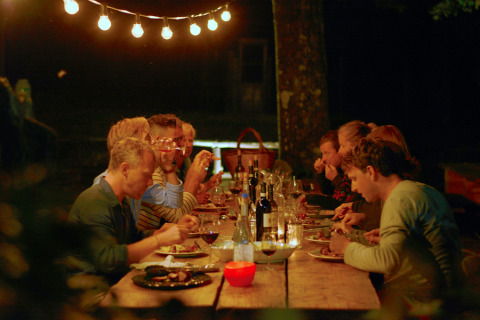 Cena all'aperto alla Novanta Skylodge, Italia, sotto luci sospese, ospiti che gustano cibo e vino insieme.