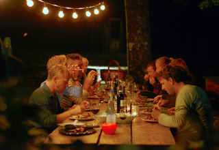 Outdoor dinner gathering at Novanta Skylodge, Italy, under string lights, with guests enjoying food and drinks.