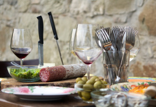 Rustic outdoor table with wine, salami, olives, and cutlery at Novanta Skylodge glamping, Italy.