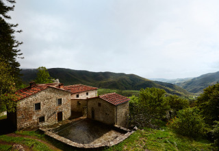 Sistemazione glamping Novanta Skylodge in Italia, casa in pietra con tetto rosso immersa nelle montagne.